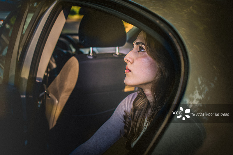 一位美丽年轻女性坐在车后座上，感到悲伤、无助和沮丧。图片素材