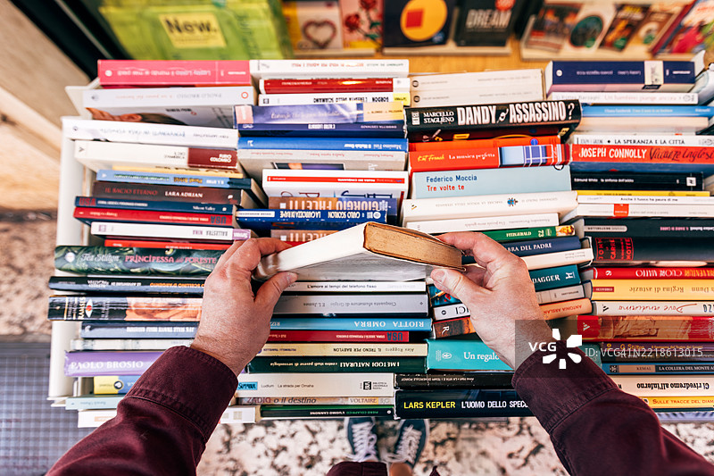 男子在户外书店展示架前挑选书籍，个人视角。图片素材