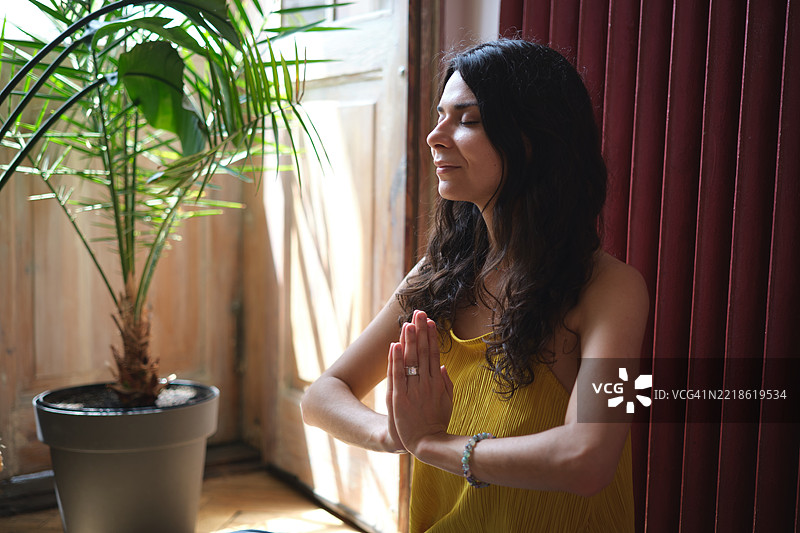 在家冥想。年轻女性坐在窗边，闭眼冥想。城市生活与心理健康图片素材