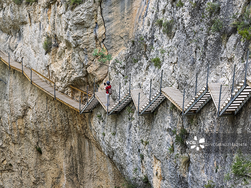冒险旅游，一名女性在峡谷岩壁嵌入的木栈道上用手机拍照。Relleu人行天桥图片素材