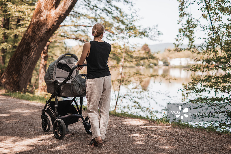 休闲装母亲在Koseski bajer城市公园推着婴儿车的背影图片素材
