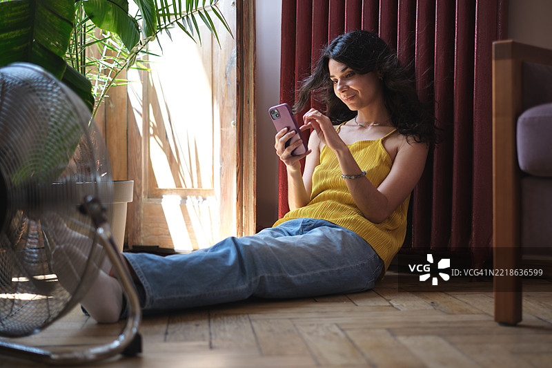 满足的女性在炎热的夏日里放松，使用电风扇享受清新空气，度过热浪时光。图片素材