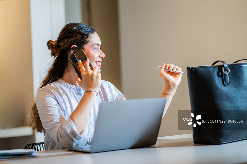 年轻女性在现代专业环境中工作并与手机通话。图片素材
