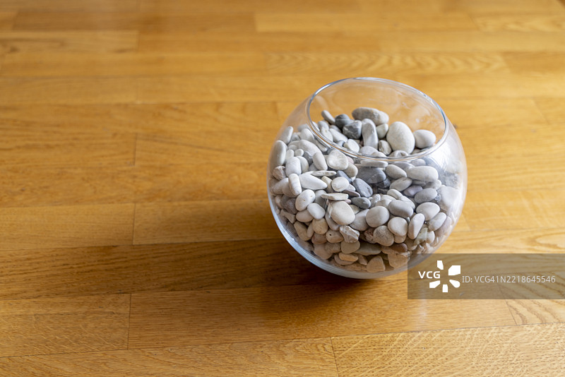 木地板上的玻璃碗里装满了白色和灰色的卵石，极简室内装饰图片素材