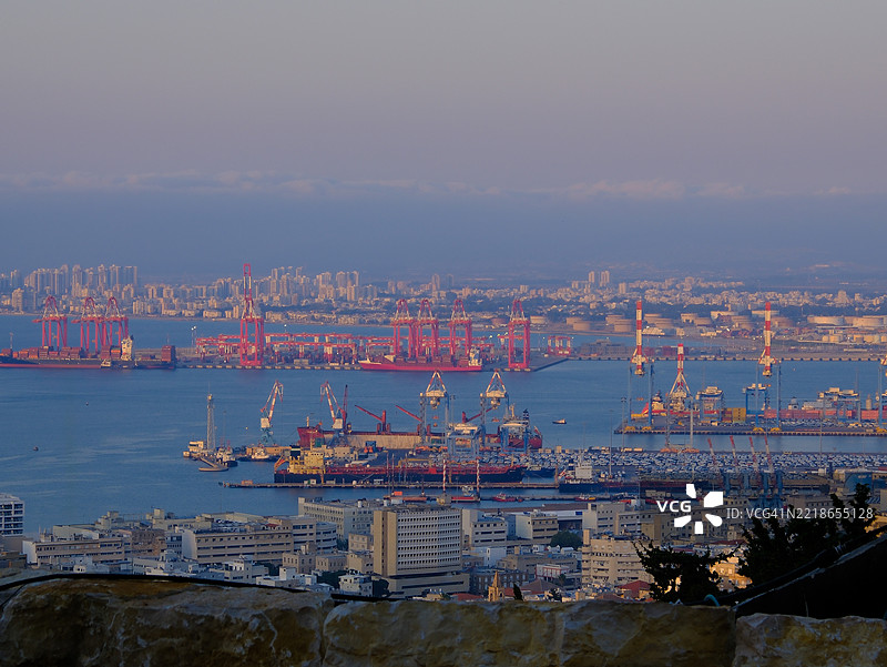 以色列海法港的全景，前景有大型货船、起重机和工业建筑，背景可见城市天际线和油罐，展示了一个繁忙的港口。图片素材