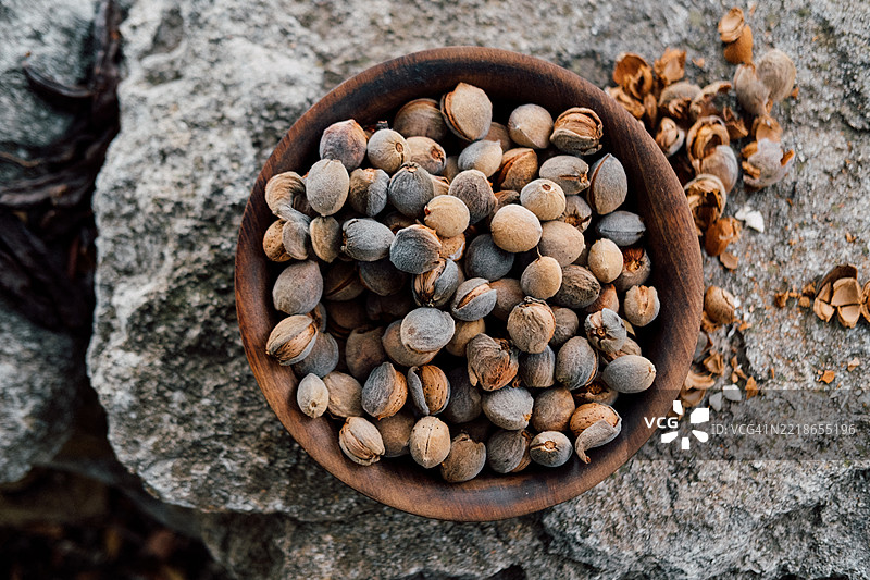 质朴的木碗里装满了天然杏仁，背景为石材。图片素材