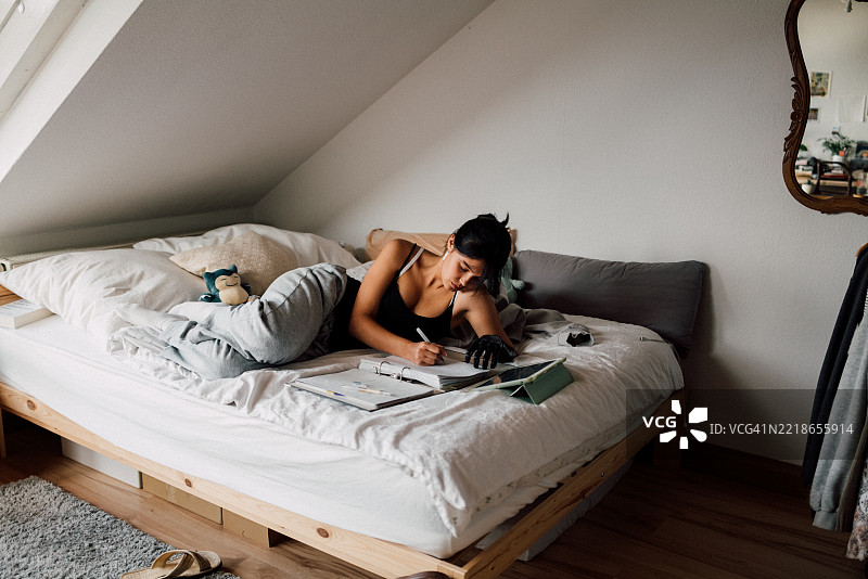 少女在舒适的卧室床上做作业图片素材