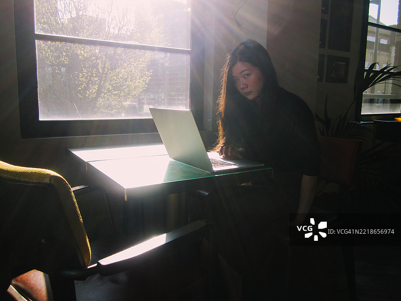 年轻的亚洲女性在阳光明媚的办公室里使用笔记本电脑图片素材