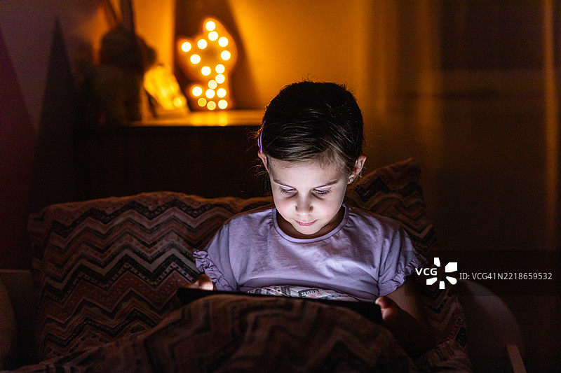 小女孩在床上夜晚看平板电脑时微笑图片素材