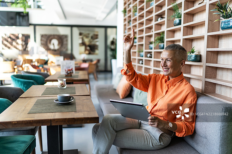 微笑的成熟的女商人在咖啡馆举手使用平板电脑图片素材
