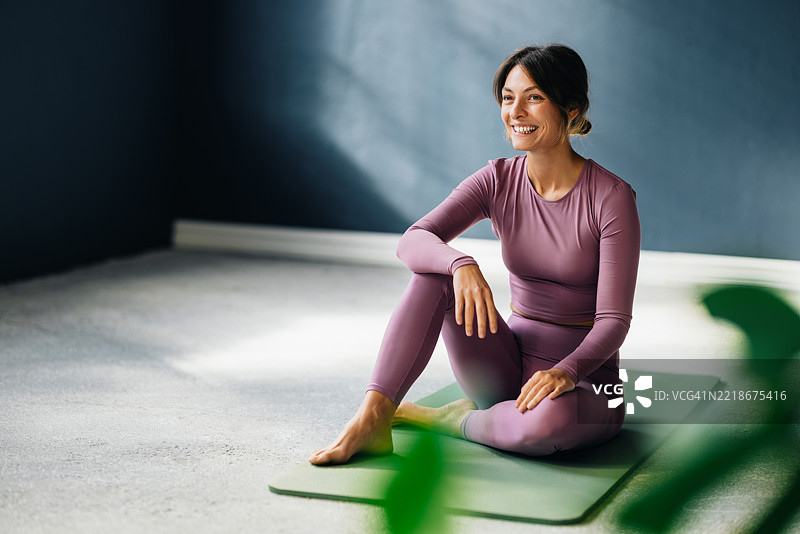微笑的女性在舒适的室内环境中练习瑜伽，坐在垫子上图片素材