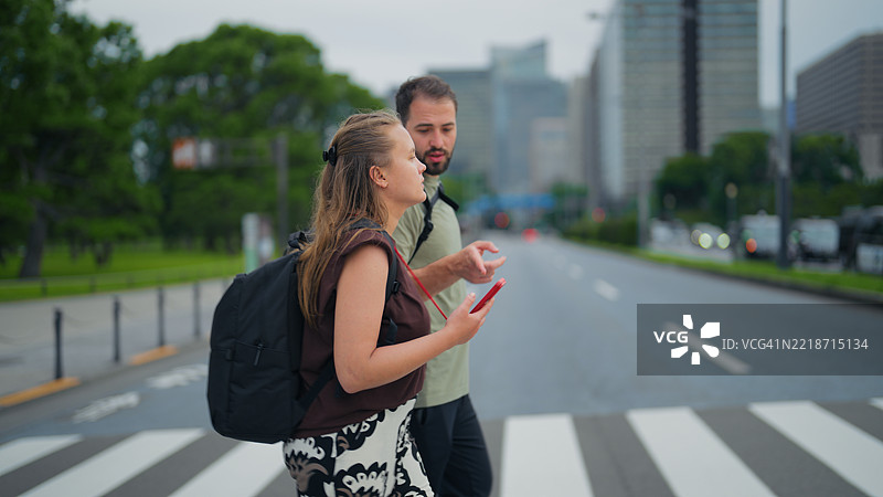 年轻情侣在东京街头走路，使用智能手机查看地图和方向图片素材