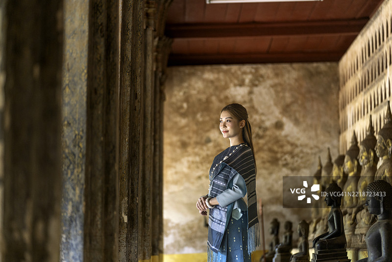 年轻的亚洲女性穿着传统老挝服装，站在老挝万象的西萨凯寺。图片素材