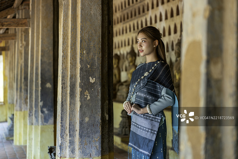 年轻的亚洲女性穿着传统老挝服装，站在老挝万象的西萨凯寺。图片素材
