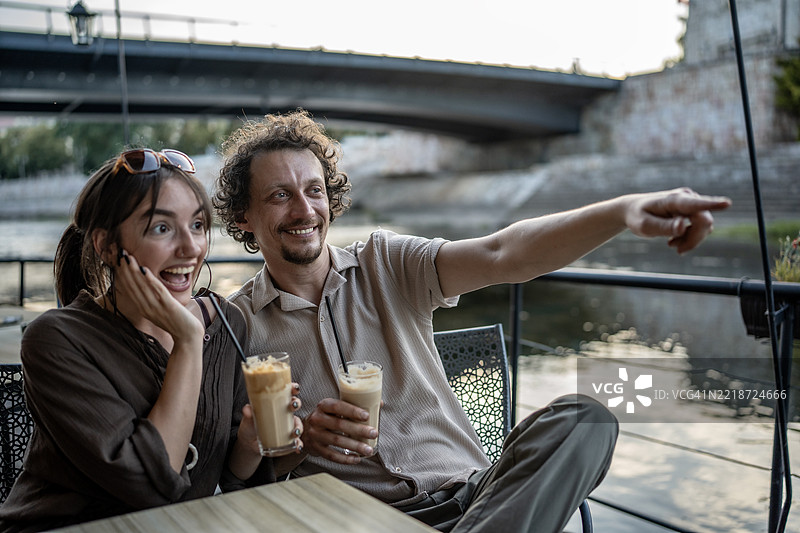 阳光明媚的日子里，微笑的情侣在河边咖啡馆享受饮品图片素材