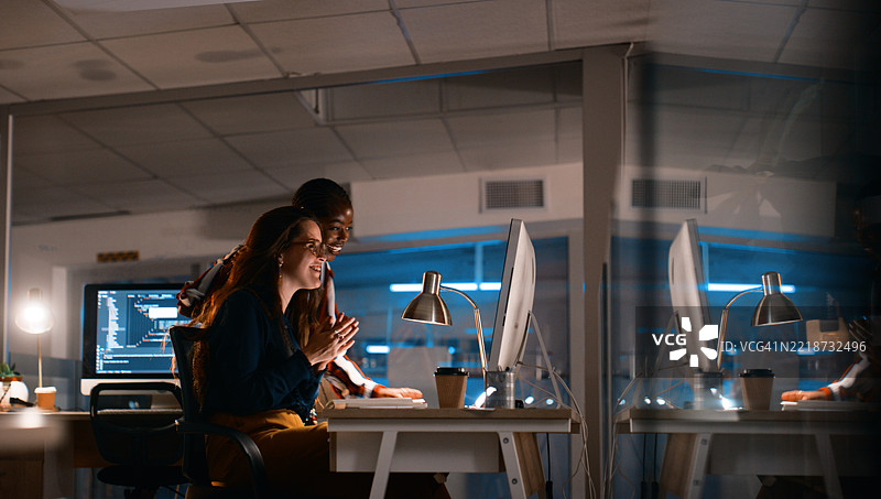 软件开发团队在办公室夜间协作，电脑屏幕和温暖的台灯照亮着工作环境图片素材