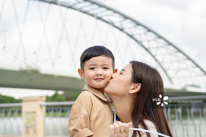 年轻母亲在户外亲吻她的儿子图片素材