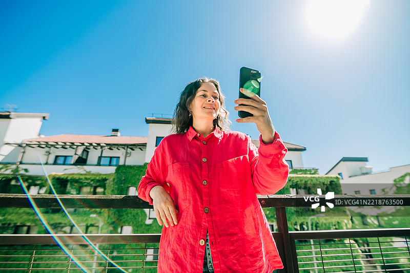 阳光明媚的城市中，女性正在使用智能手机图片素材