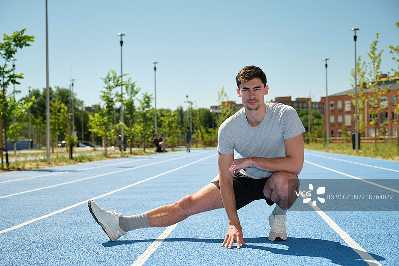 年轻运动员在蓝色跑道上拉伸腿部图片素材