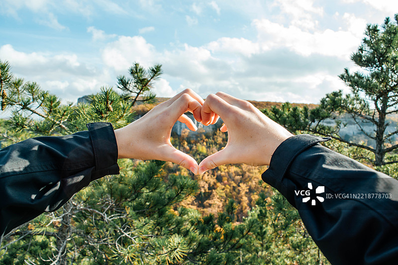 双手在美丽的秋季山景中形成一个心形。图片素材