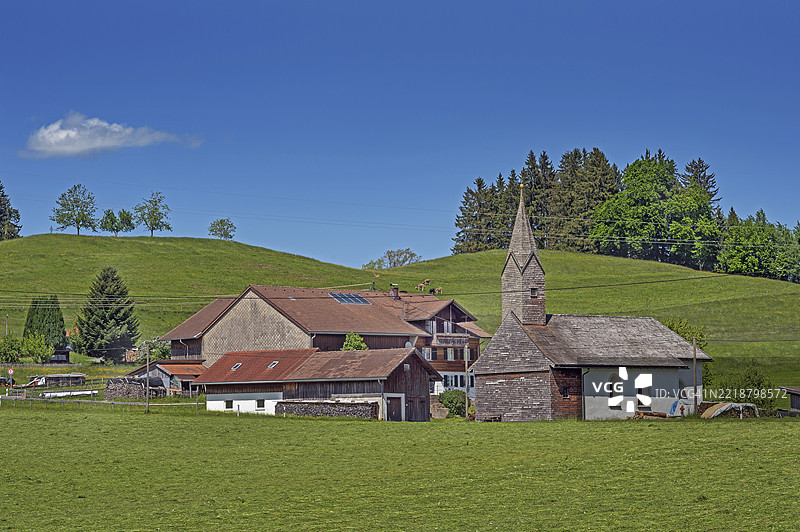 林森附近的春季割草草地、混合森林、十四世纪的圣尼古拉斯和圣玛格达莱娜小教堂，屋顶覆盖着许多木瓦，位于德国巴伐利亚的阿尔高地区。图片素材