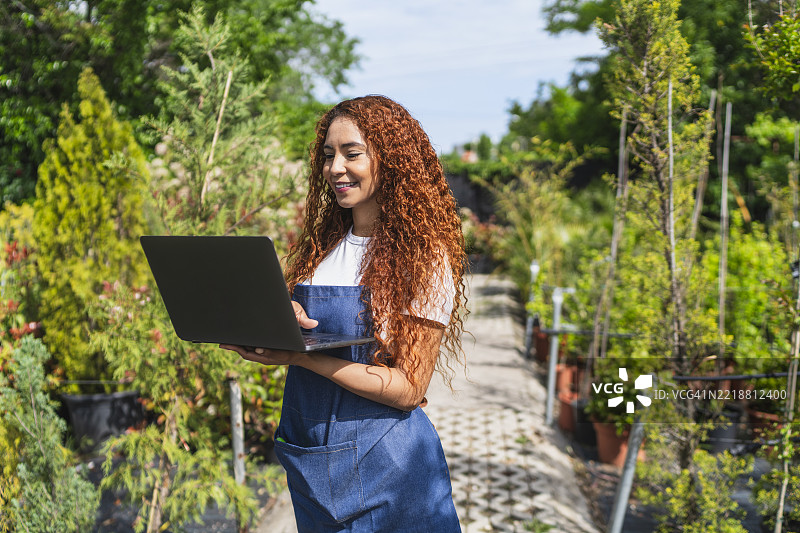 女园丁在植物苗圃中使用笔记本电脑图片素材