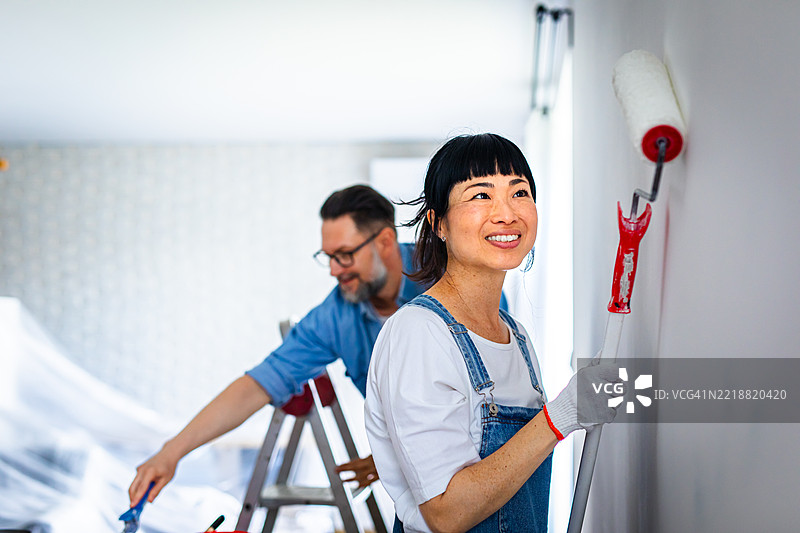 快乐的情侣在家居装修期间一起粉刷墙壁，微笑着享受DIY项目。图片素材