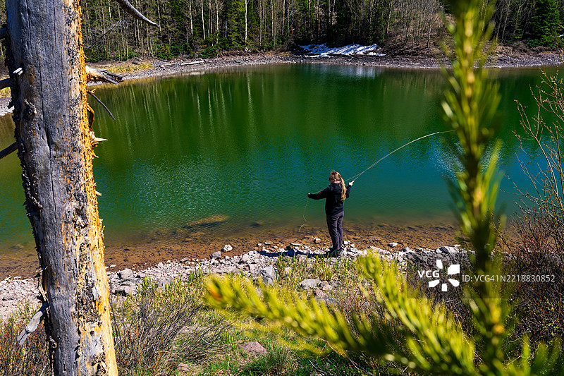 年轻女性在高山湖泊中投掷飞钓竿图片素材