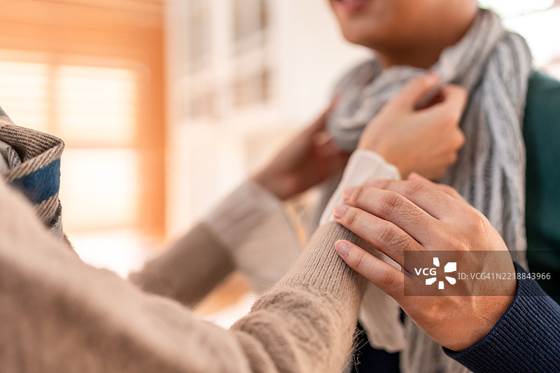 年轻夫妇在冬季的家中享受温馨时光的特写。迷人的妻子为丈夫系上温暖的围巾，感到快乐和放松，舒适地站在厨房里。图片素材