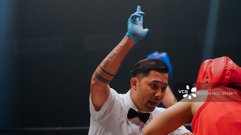 年轻的亚洲拳击裁判正在为一位在拳击回合中摔倒的女拳手数数。图片素材