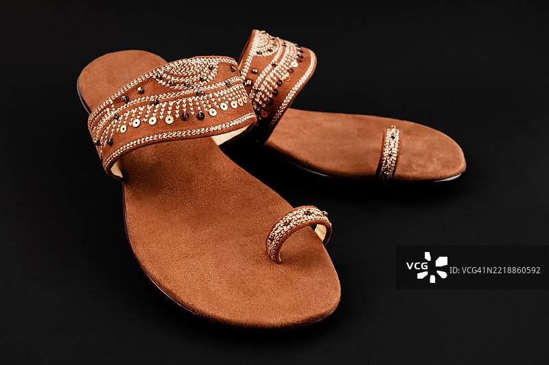 一双棕色凉鞋放在黑色背景上。女性鞋子极简风格。图片素材