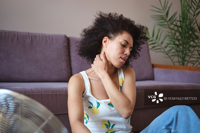 夏季炎热。过热的非裔美国女性在家中使用电风扇，卷发女孩坐在地板上在热浪中降温。图片素材