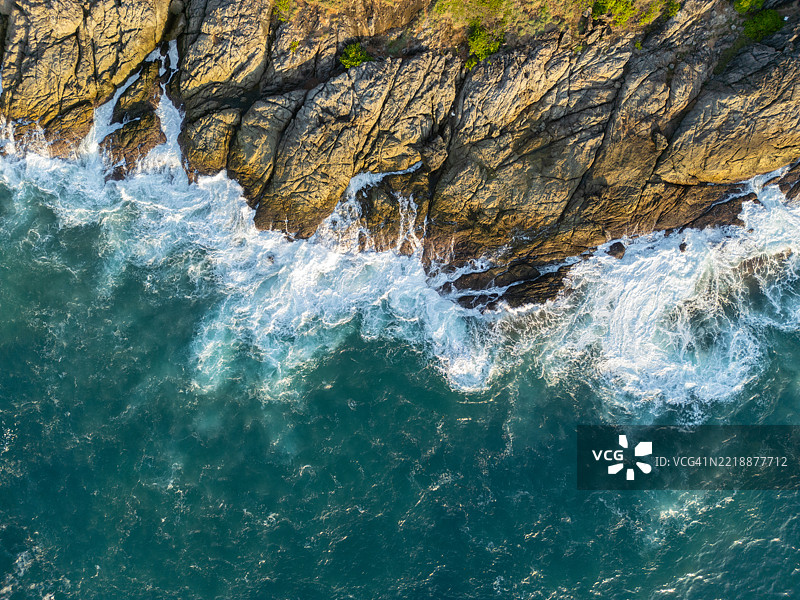 陡峭的岩石悬崖上方，波浪在下面猛烈撞击图片素材
