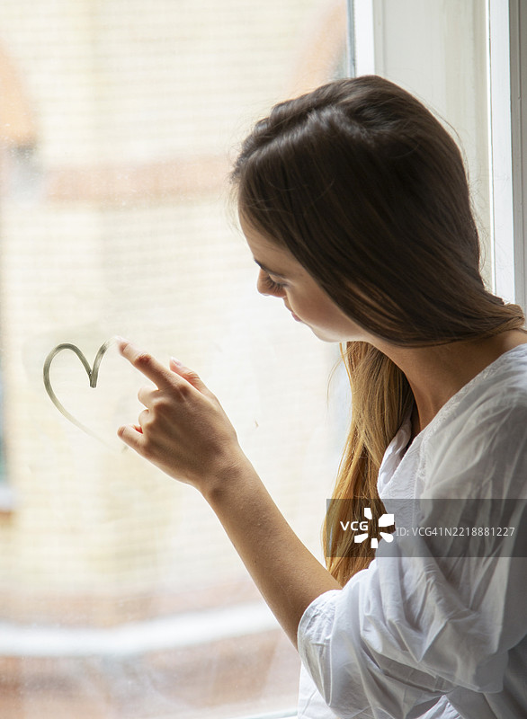 年轻女性在窗玻璃上画心形图案图片素材
