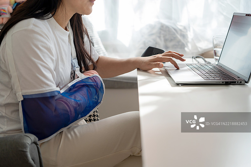 手臂打着石膏的女商人在家中坐着工作图片素材