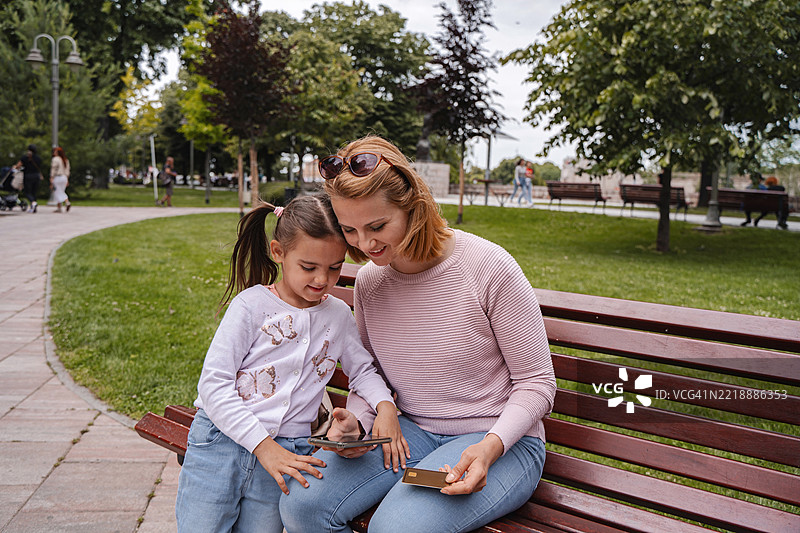 母女在公园里使用智能手机和信用卡进行在线购物图片素材