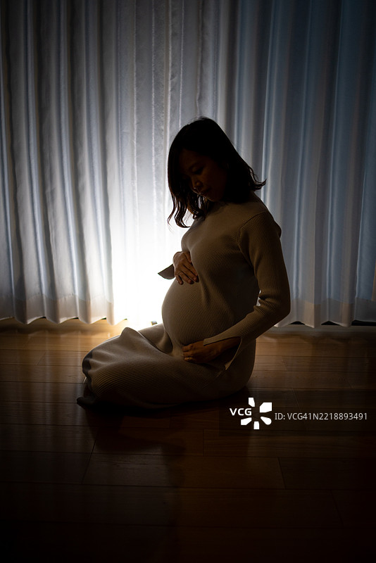 怀孕的女人坐在昏暗的客厅里，呈现剪影状态图片素材