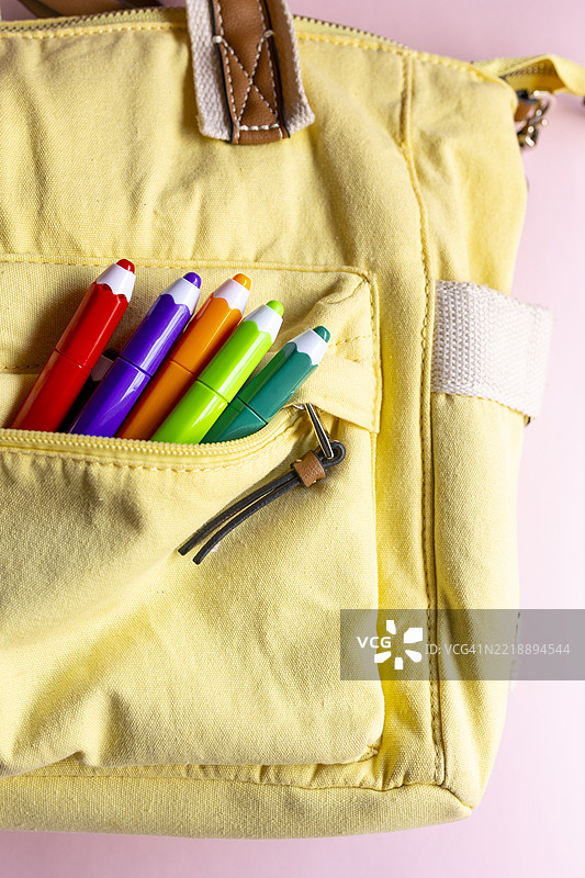 黄色的书包配有五彩铅笔形状的笔，适合开学使用图片素材