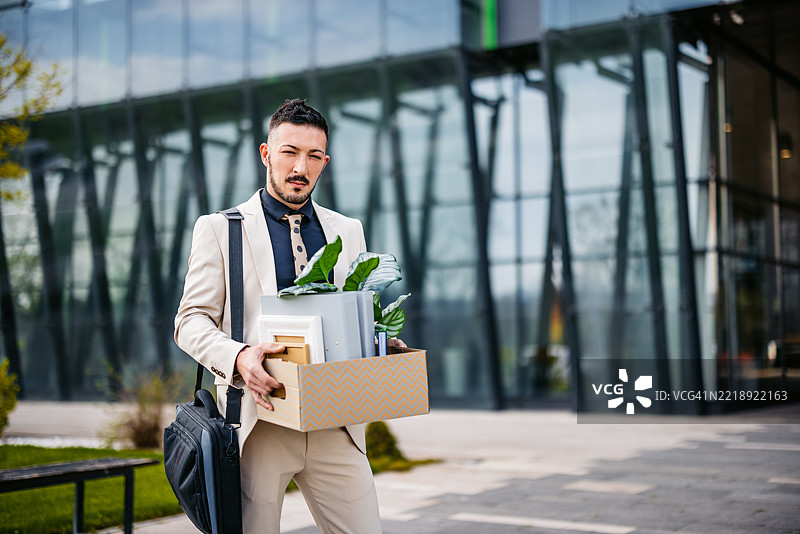悲伤的中年商人手里拿着办公桌上的物品，站在一座企业大楼前图片素材