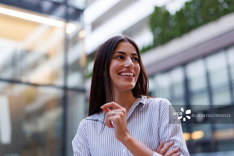 一位愉快的女商人在城市环境中微笑并望向远方的肖像图片素材