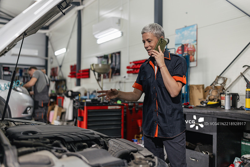 在繁忙的汽车修理店里接电话的机械师图片素材