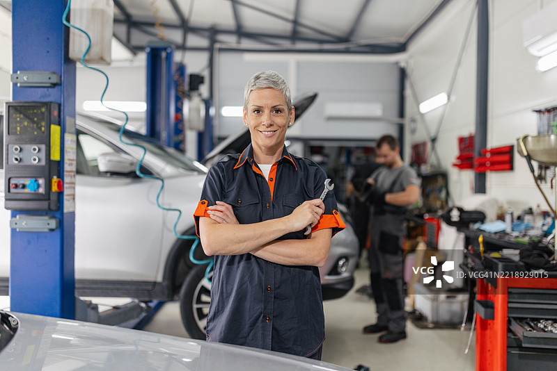 自信的机械师在汽车旁摆姿势，手持工具。图片素材