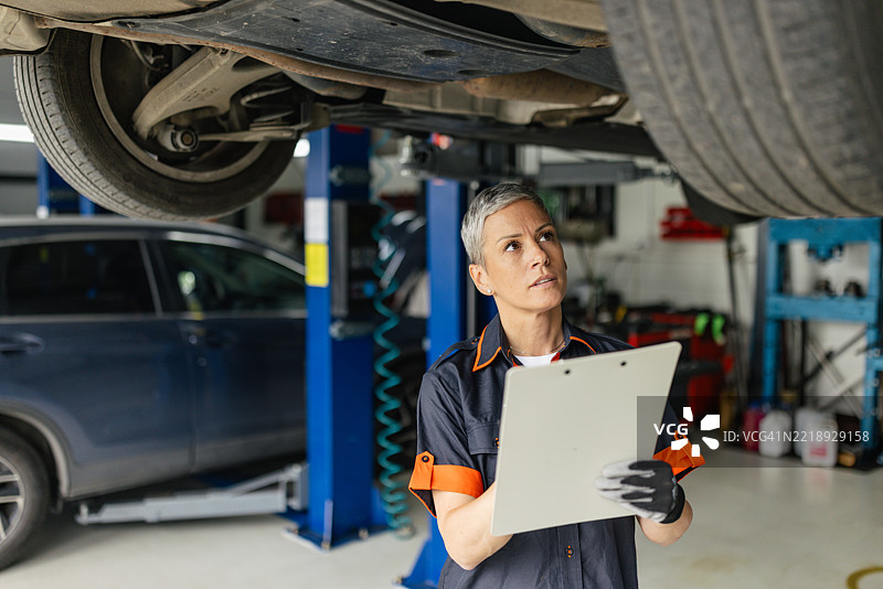 女性在车间的升降机下检查车辆图片素材