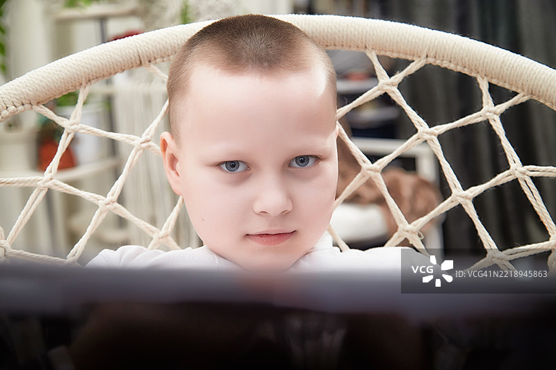 孩子坐在家里的挂绳椅上专注于屏幕图片素材