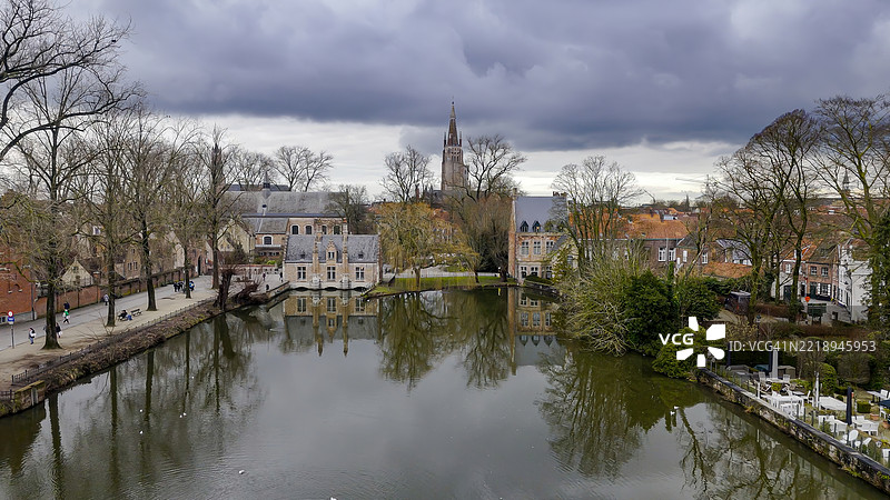 布鲁日的Wijngaardplein鸟瞰图，展现了运河、天鹅、步行桥和历史悠久的弗拉芒建筑，宁静的城市遗产与自然的融合，适合欧洲旅行和文化故事讲述的电影级无人机镜头。图片素材
