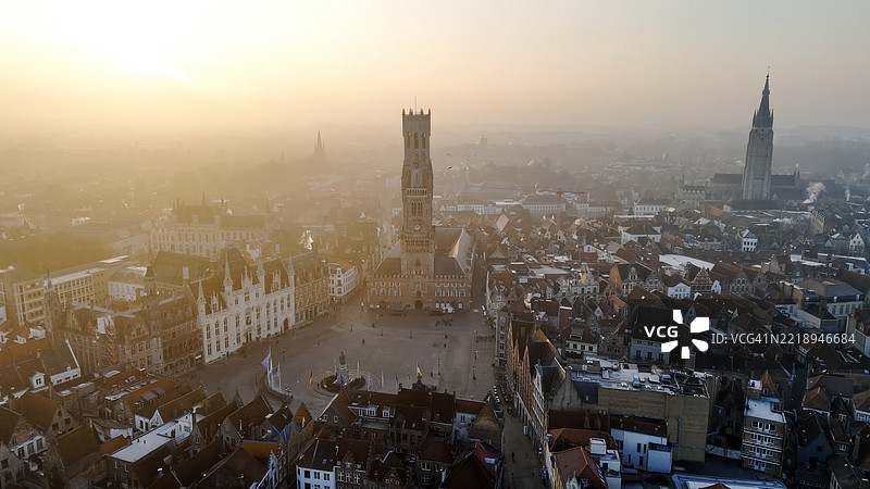 布鲁日钟楼和历史悠久的市场广场在日出时的鸟瞰图，标志性的中世纪钟楼和弗拉芒建筑，城市遗产与旅行设计概念，温暖晨光下的全景城市风光图片素材