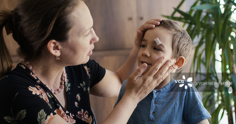 母亲照顾眉毛上有伤口的儿子图片素材