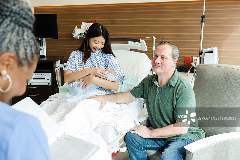 快乐的新父母在医院房间里抱着他们的新生儿图片素材