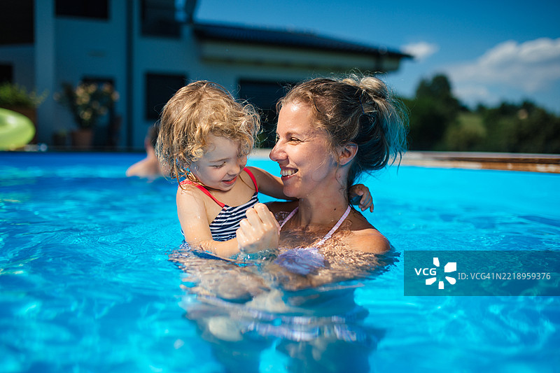 妈妈和小女儿在水中玩耍。家庭在后院游泳池中享受乐趣。图片素材
