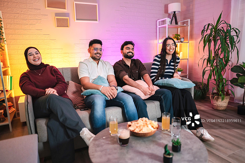 四个朋友在色彩缤纷的客厅里看电视，享受零食和饮料。图片素材